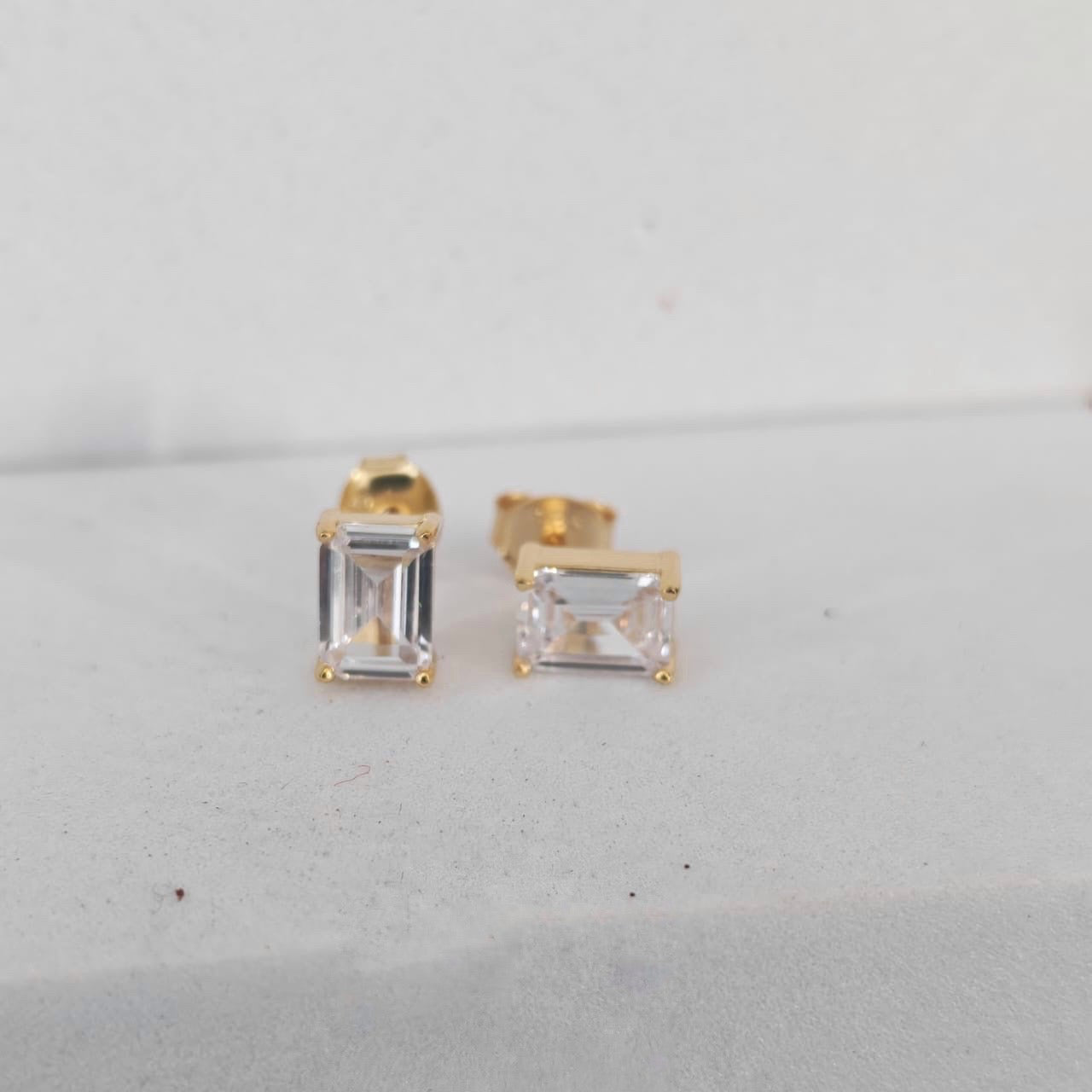 Gold stud earrings with clear gemstones on a light gray background