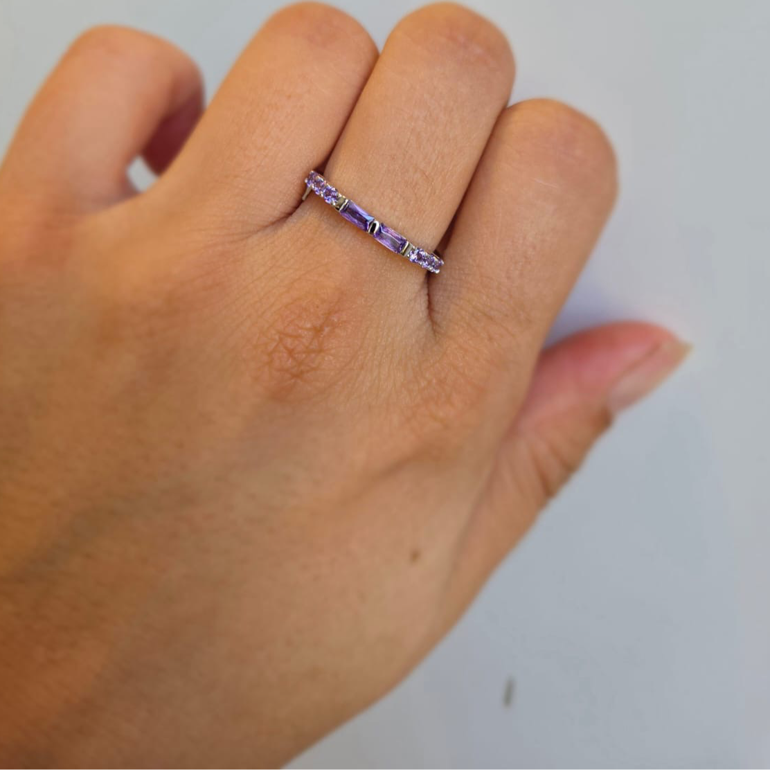 A purple stacking ring made of sterling silver with purple cubic zirconia, worn on a person's hand.