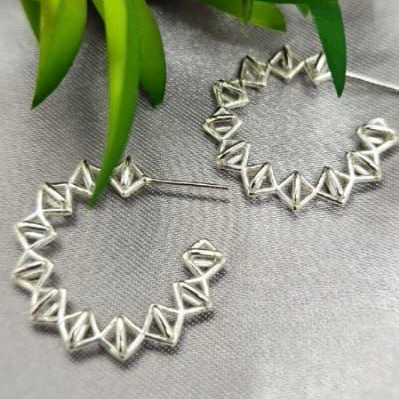 Silver hoop earrings on a gray surface with green leaves in the background