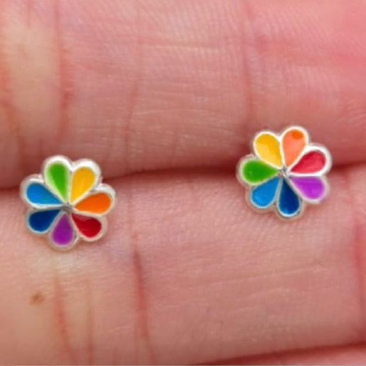 Colorful flower-shaped earrings held between fingers on a light skin background