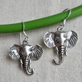 Silver elephant earrings on a green stick against a beige background