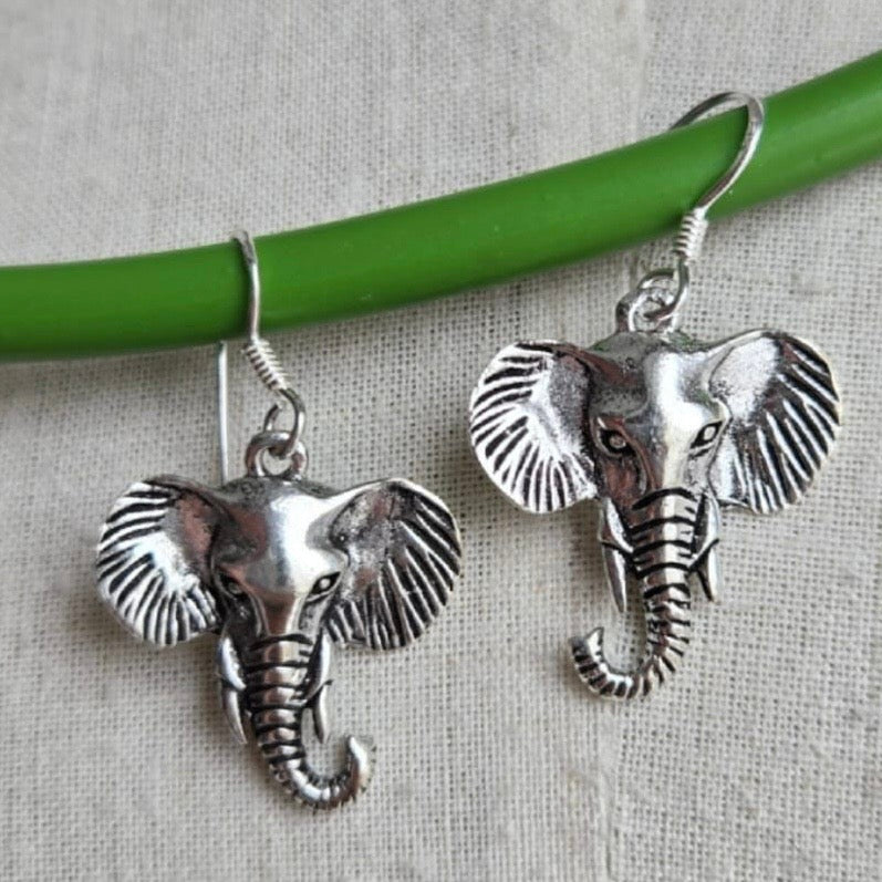 Silver elephant earrings on a green stick against a beige background