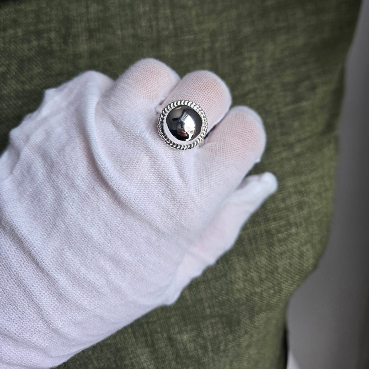 Silver button on a white glove with a green fabric background