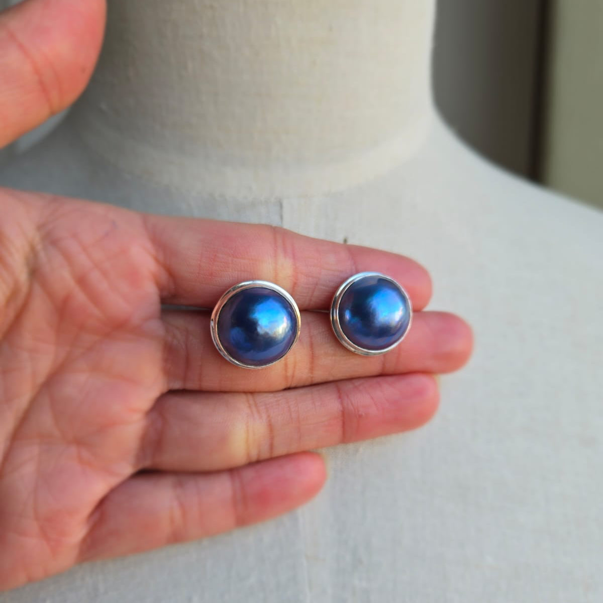 Blue round earrings held between fingers on a neutral background