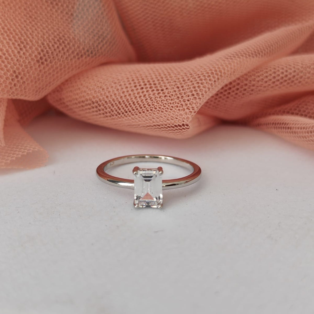 Silver ring with a diamond on a white surface with pink fabric in the background