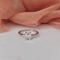 Silver ring with a diamond on a white surface with pink fabric in the background