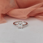 Silver ring with a diamond on a white surface with pink fabric in the background
