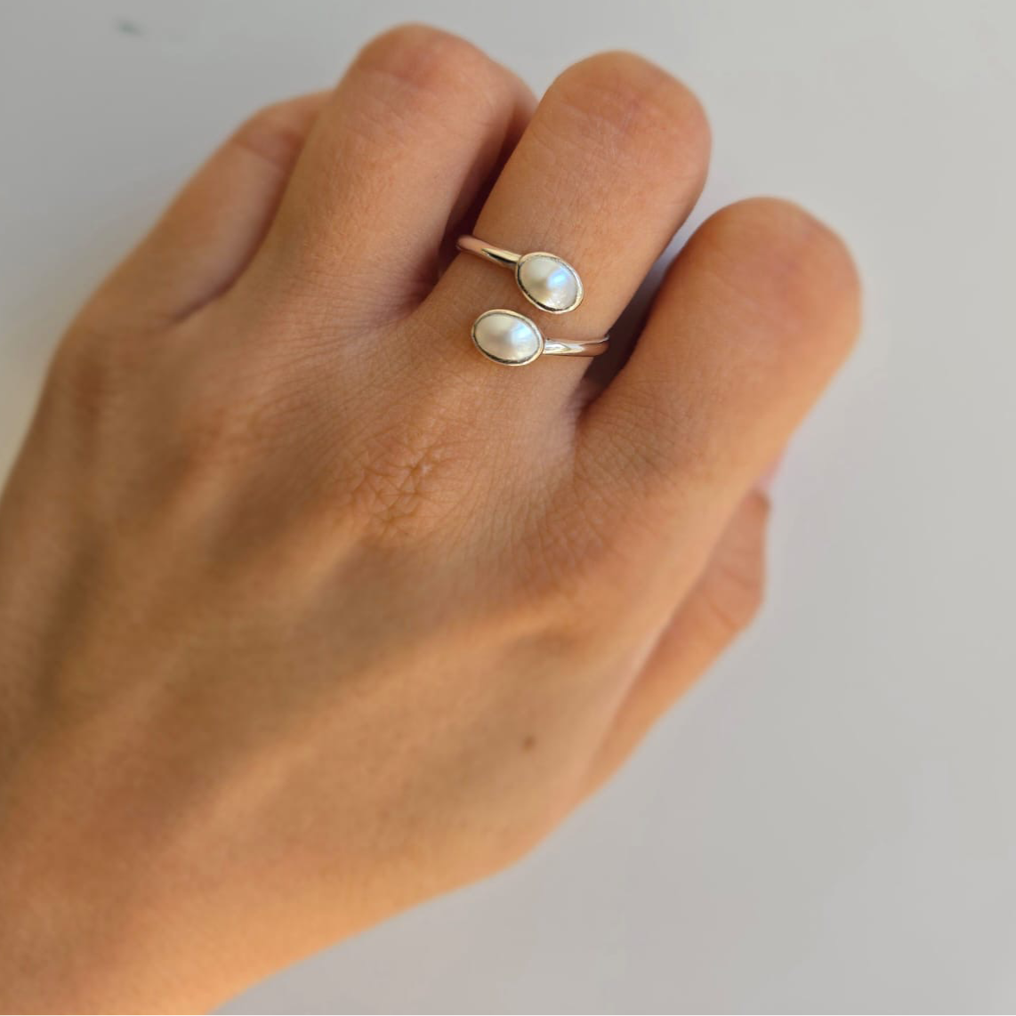 An open size two pearl ring with sterling silver band, worn on a person's finger.