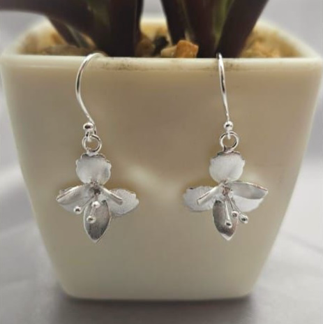 A pair of sterling silver drop flower earrings displayed on a table next to a white vase with a green plant.