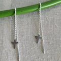 Silver cross necklace on a green stick against a textured gray background