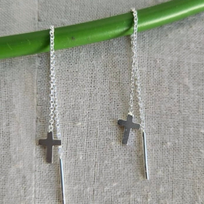 Silver cross necklace on a green stick against a textured gray background