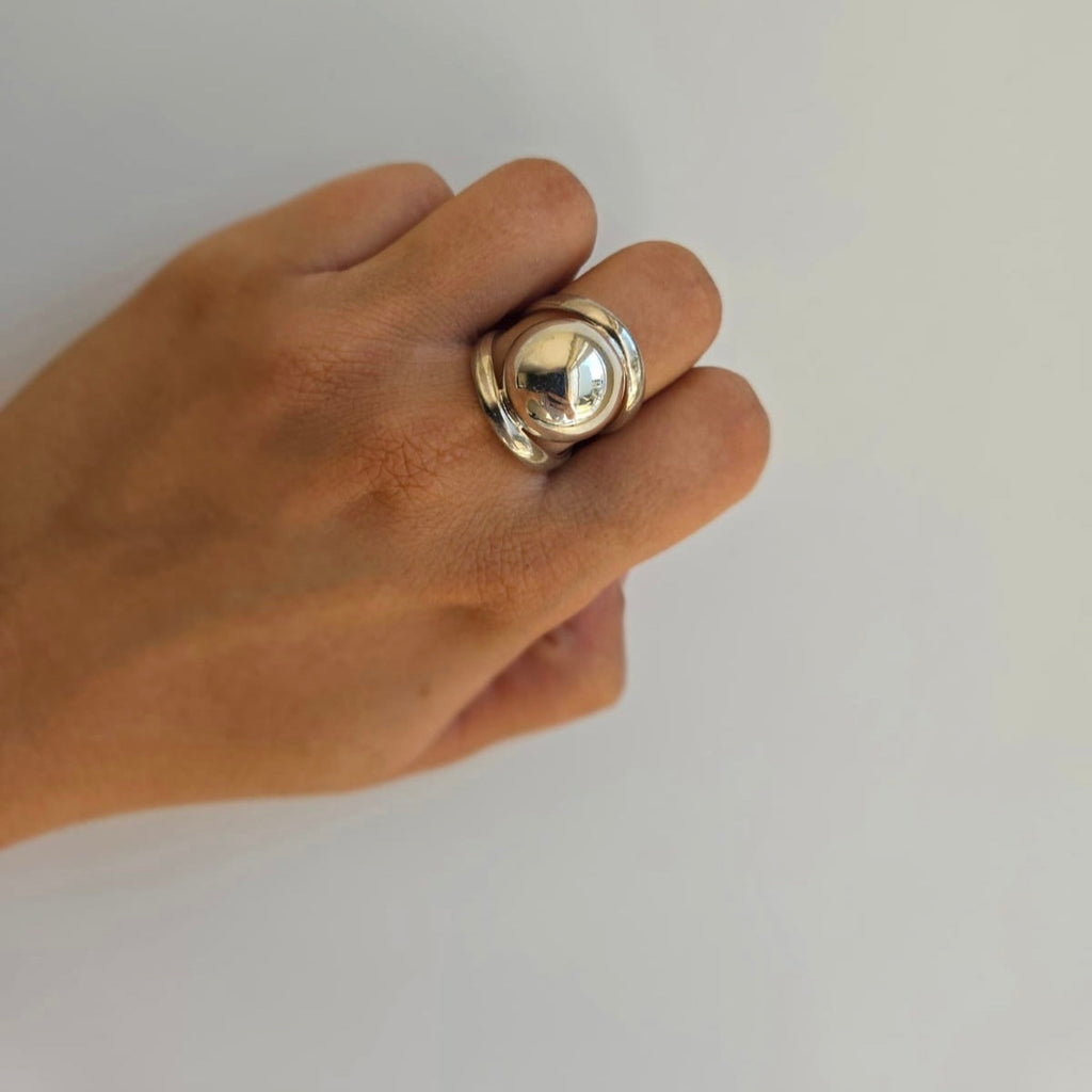 A sterling silver ball ring on a person's finger, with a polished surface and a reflective shine.