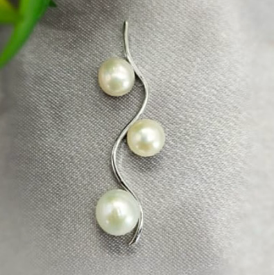 A sterling silver pendant with three freshwater pearls, displayed on a textured background.