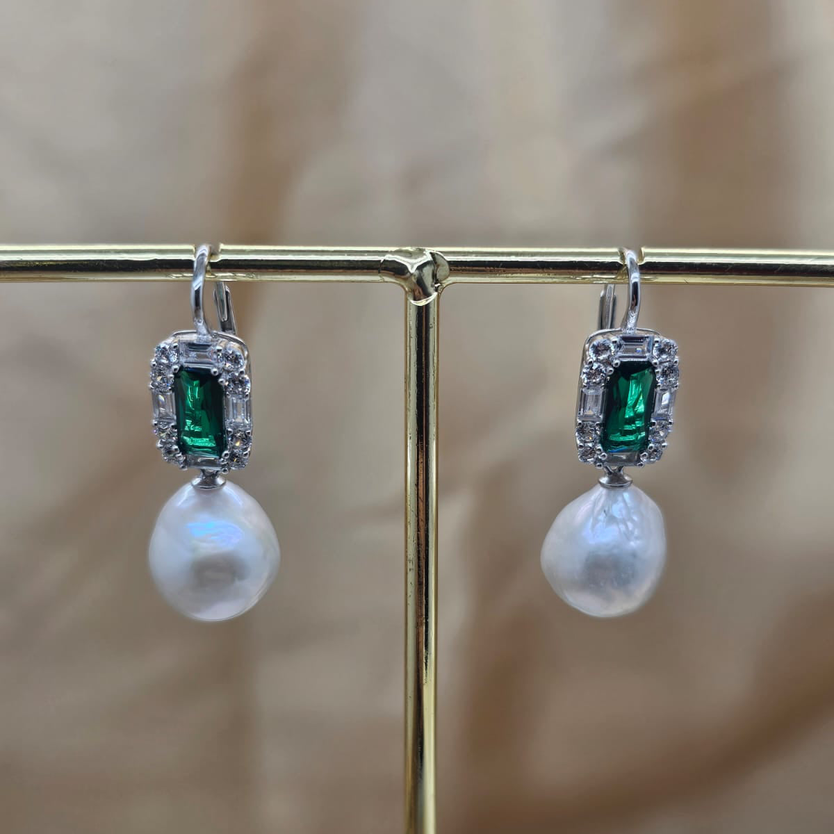 Pair of earrings with green gemstones and pearl drops on a stand.