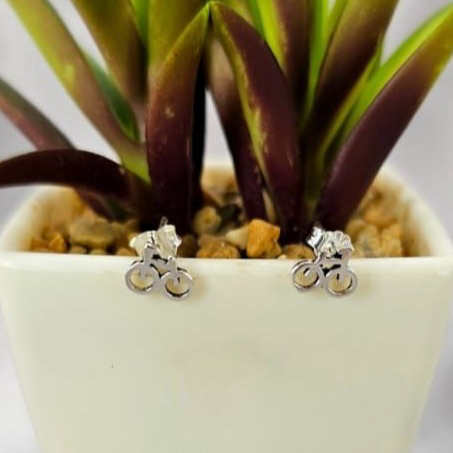 A pair of sterling silver bicycle-shaped stud earrings displayed in front of a potted plant.