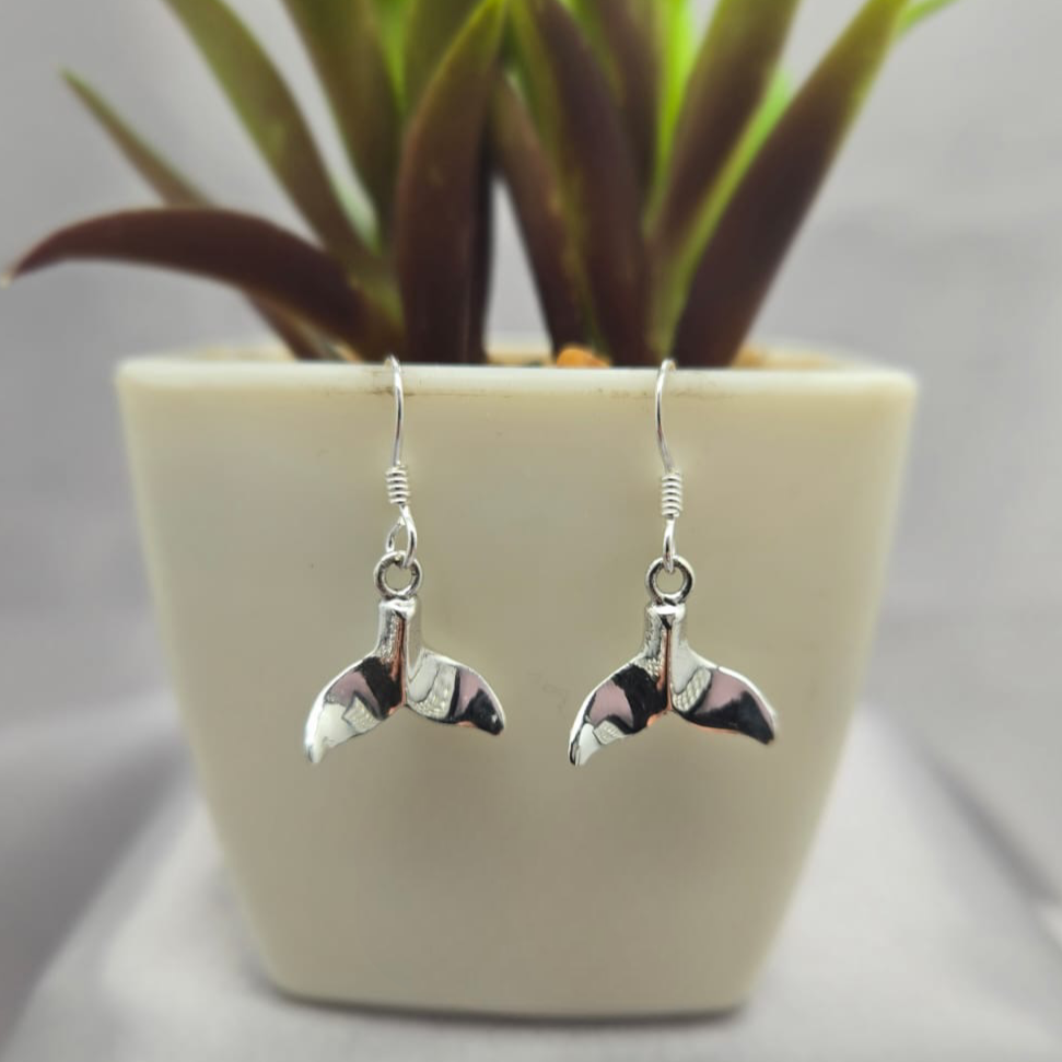 Silver bird-shaped earrings on a gray surface with a potted plant in the background