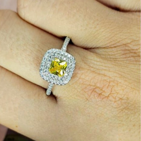 A hand holding a sterling silver square ring with a yellow cubic zirconia centre, with a clear and bright appearance.
