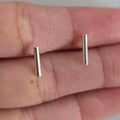 Two silver bar earrings held between fingers on a neutral background