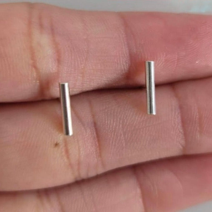 Two silver bar earrings held between fingers on a neutral background