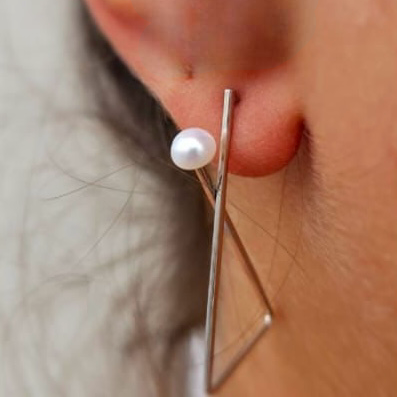 A close-up image of a person's ear wearing a sterling silver hoop earring with a freshwater pearl on the end.