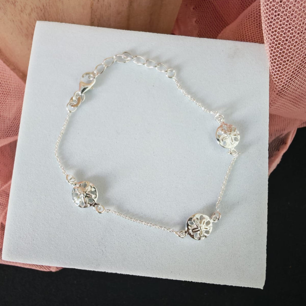 Silver bracelet with floral designs on a white card held by a person wearing pink gloves.