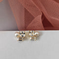 Pair of pearl and crystal stud earrings on a light gray surface with pink fabric in the background.
