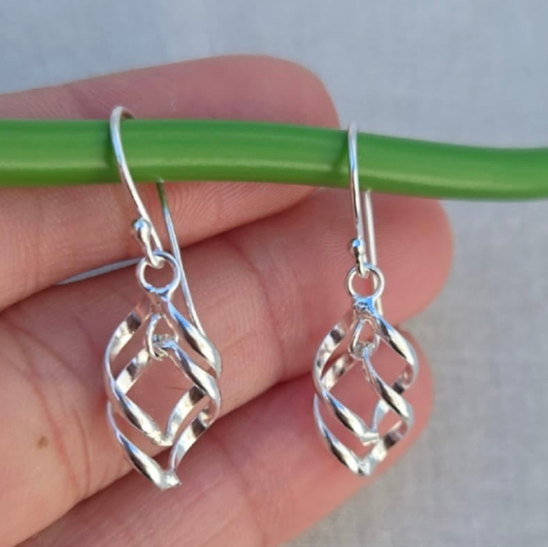 Silver earrings held against a neutral background