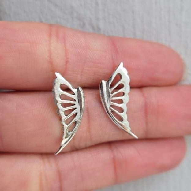Silver butterfly wing earrings held between fingers against a neutral background