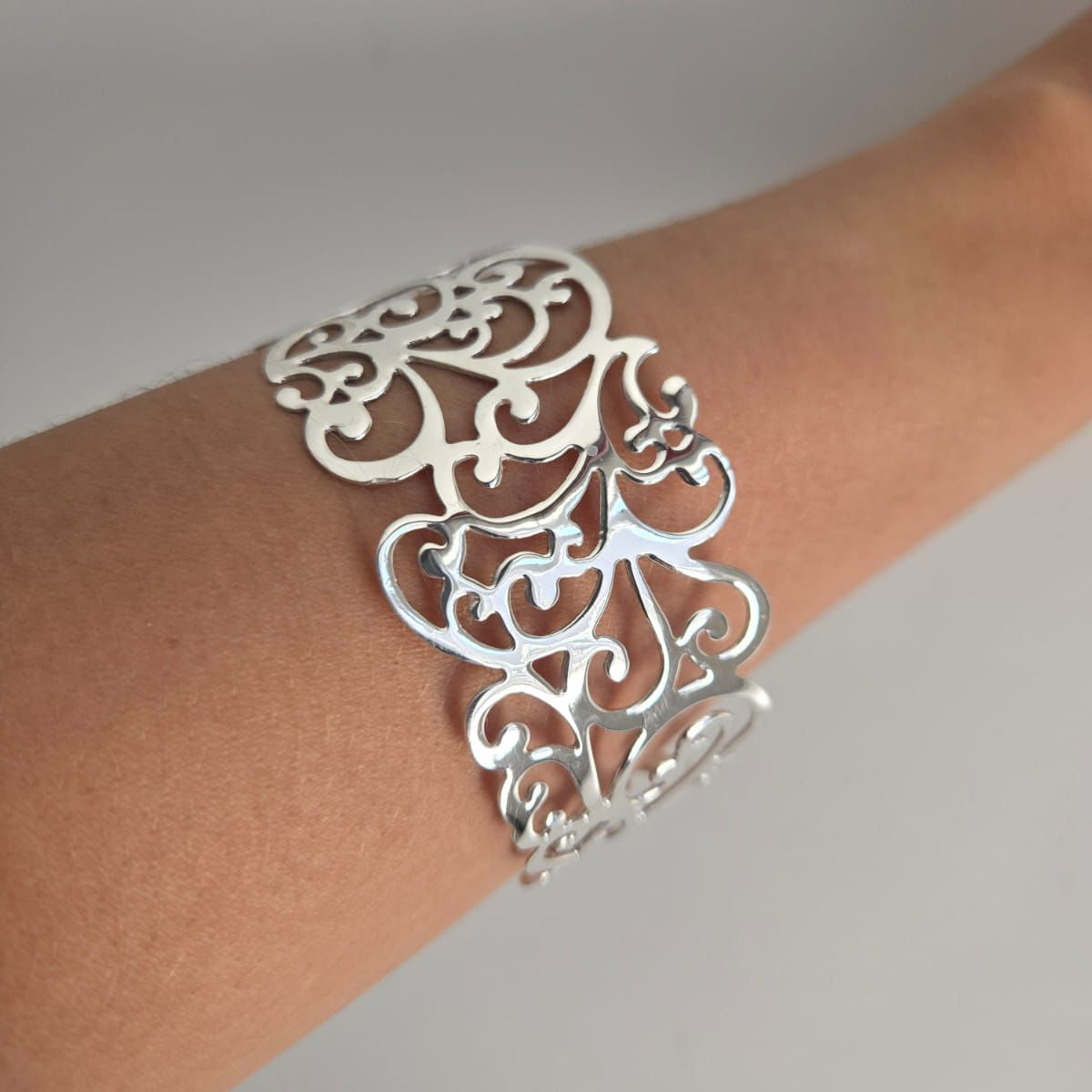 Silver filigree bracelet on a wrist against a neutral background