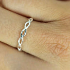 A sterling silver 'koeksister' band ring worn on a person's finger, displaying a braided design.