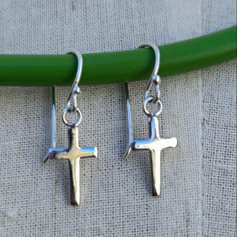 Silver cross earrings hanging from a green rod on a textured gray background
