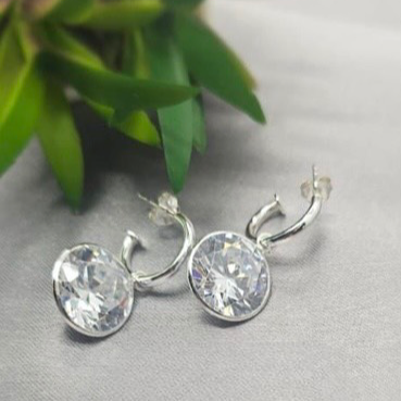 A pair of sterling silver hoop earrings with clear cubic zirconia stones, displayed against a neutral background with a green plant.