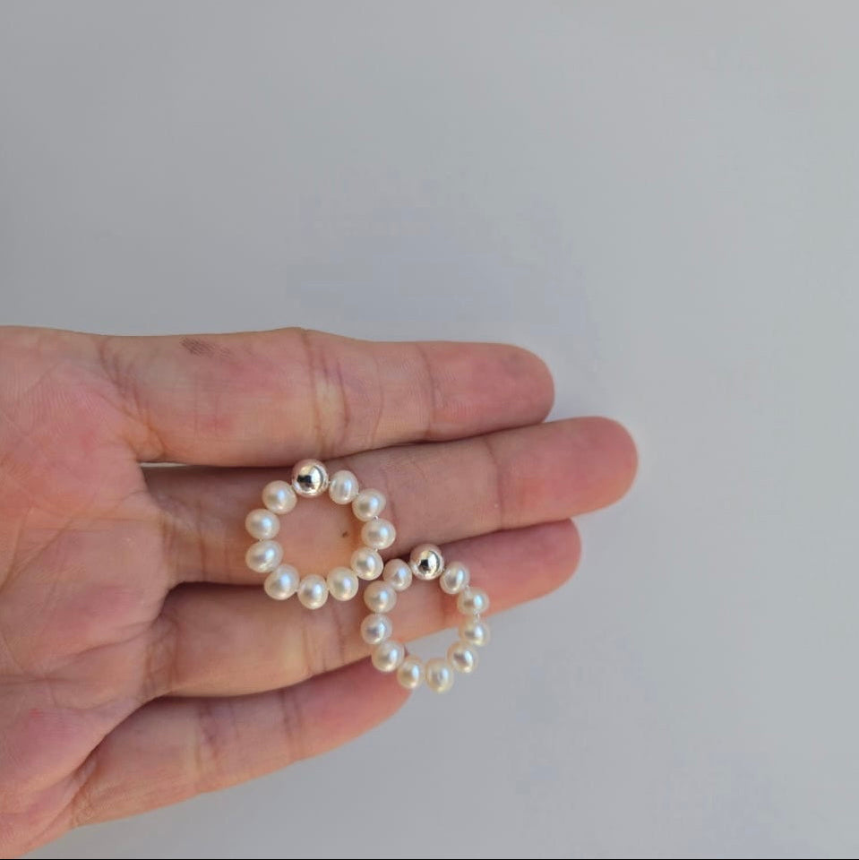 A pair of 18mm Freshwater pearl hoop earrings on a stud, held between fingers against a neutral background.