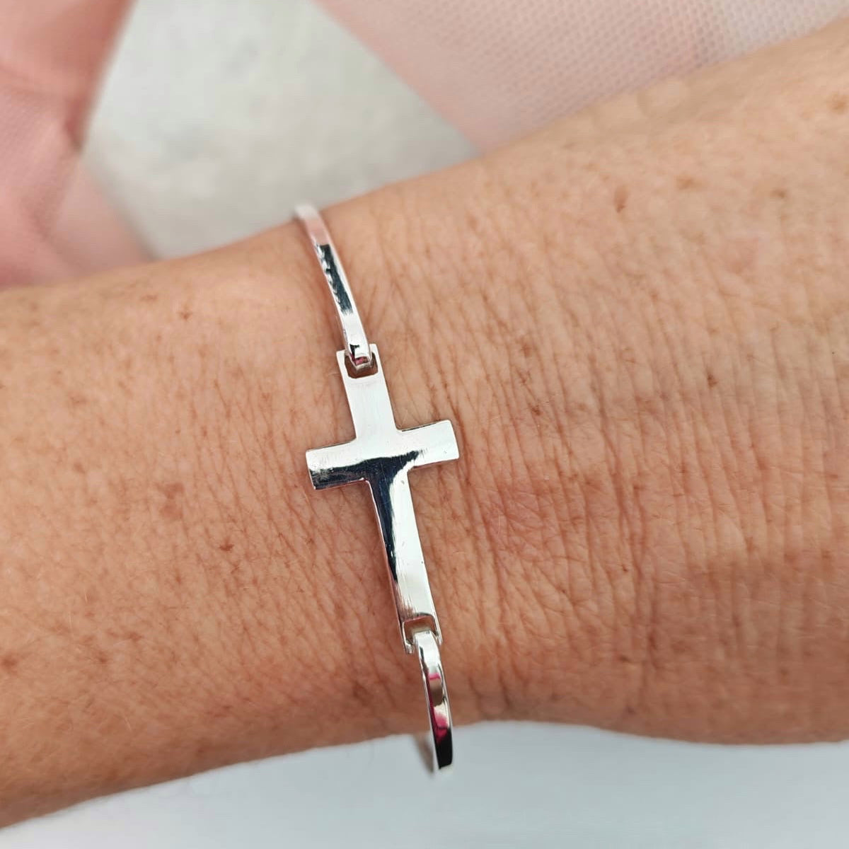 Silver bracelet with a cross charm on a wrist against a neutral background