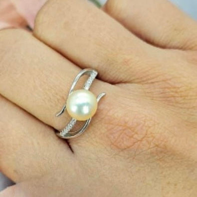 An adjustable ring with a freshwater pearl centerpiece, displayed on a person's hand.