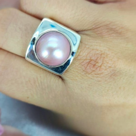 A pink Mabe pearl ring in a sterling silver square setting, displayed on a person's finger.