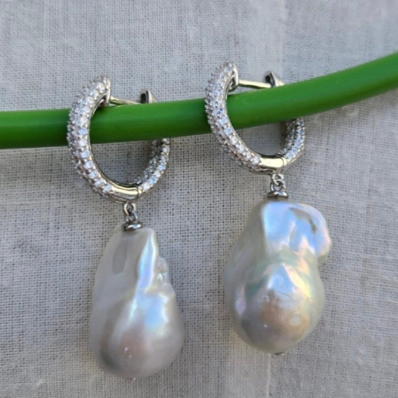 Pearl earrings with silver hoop designs on a gray background