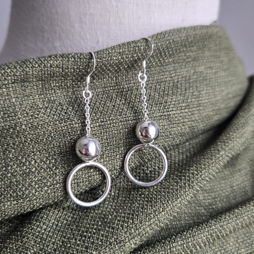 Silver circle earrings on a mannequin with a green fabric background