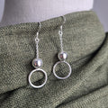 Silver circle earrings on a mannequin with a green fabric background