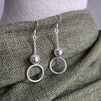 Silver circle earrings on a mannequin with a green fabric background