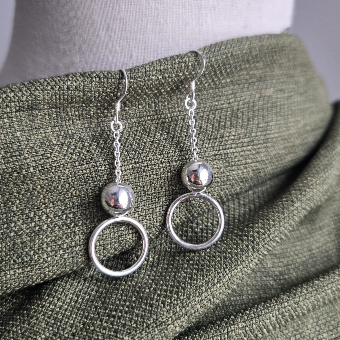 Silver circle earrings on a mannequin with a green fabric background