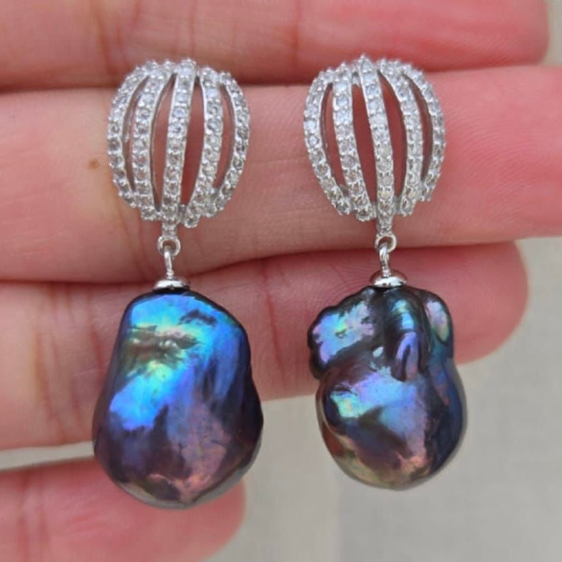 Pair of earrings with dark blue gemstones held between fingers