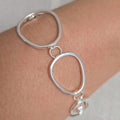 Silver bracelet with interlocking loops on a wrist against a neutral background