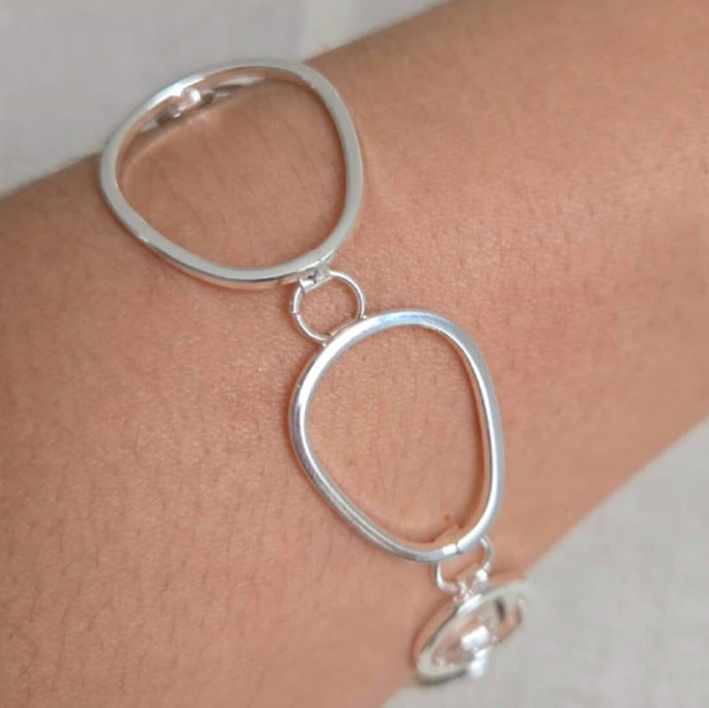 Silver bracelet with interlocking loops on a wrist against a neutral background