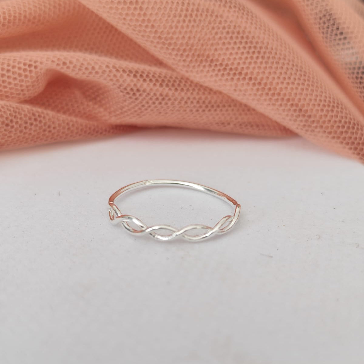 Silver twisted ring on a light pink fabric background