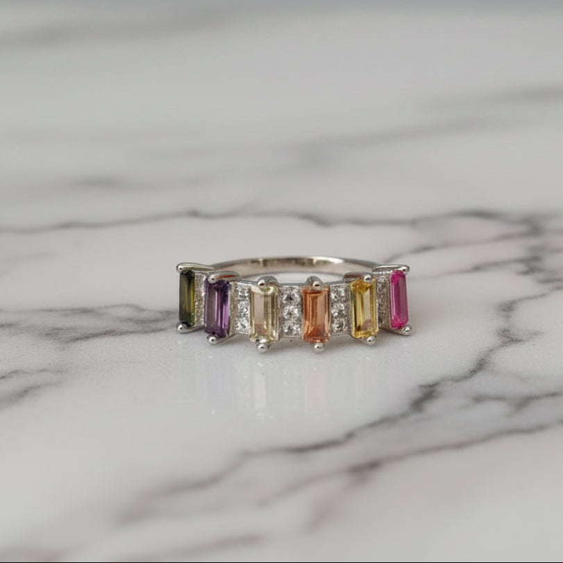 Ring with multicolored gemstones on a white surface with pink fabric in the background
