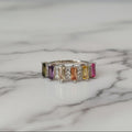 Ring with multicolored gemstones on a white surface with pink fabric in the background