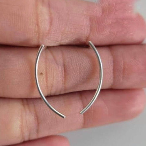 Silver hoop earrings held between fingers against a neutral background