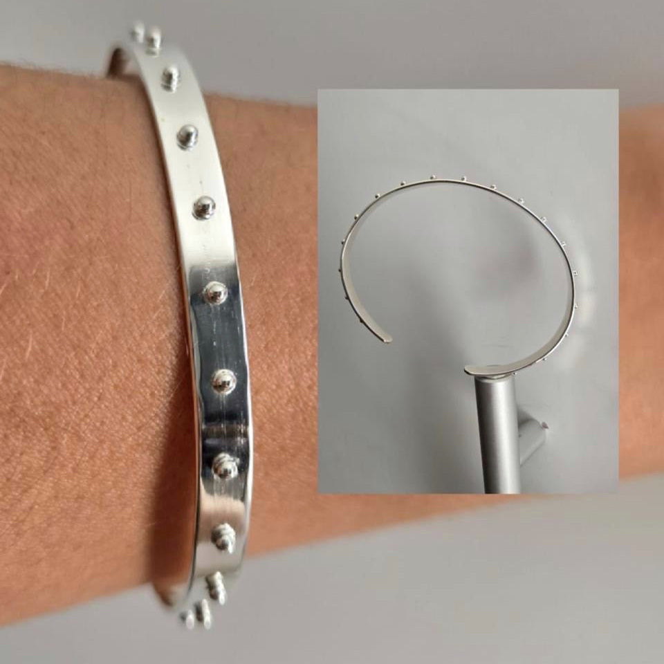 Silver bracelet on a wrist with an inset showing a close-up of the bracelet's design.