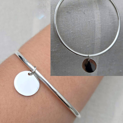 Silver bangle with a round pendant on a wrist, close-up inset showing the bangle.